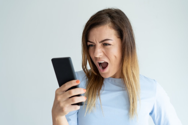 Mujer enojada gritando en el teléfono inteligente. Señora indignada que usa el dispositivo.