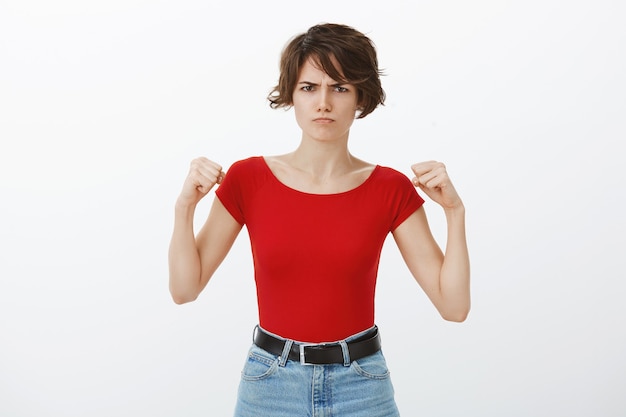 Mujer enojada linda que hace pucheros hirviendo de ira, levantando los puños y enfurruñada enojada