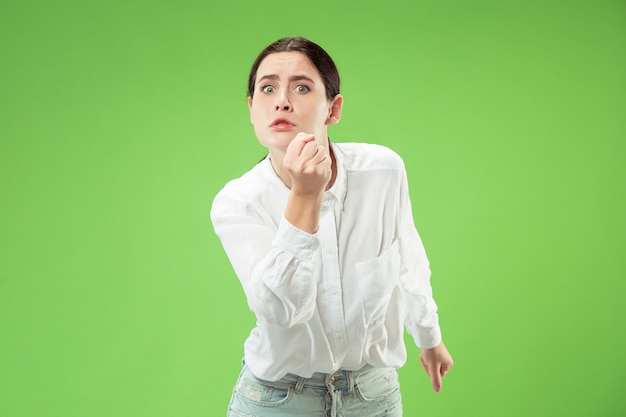 Mujer enojada mirando a cámara. Mujer de negocios agresiva que se encuentran aisladas sobre fondo de moda estudio verde. Retrato femenino de medio cuerpo. Las emociones humanas, el concepto de expresión facial.