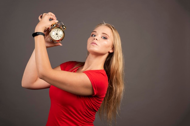 Mujer enojada posando con reloj sobre fondo oscuro. Foto de alta calidad