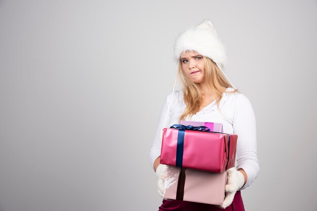 Mujer enojada con regalos de Navidad en la pared gris.