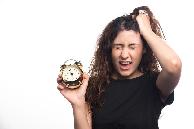 Mujer enojada sosteniendo su cabello y reloj sobre fondo blanco. Foto de alta calidad