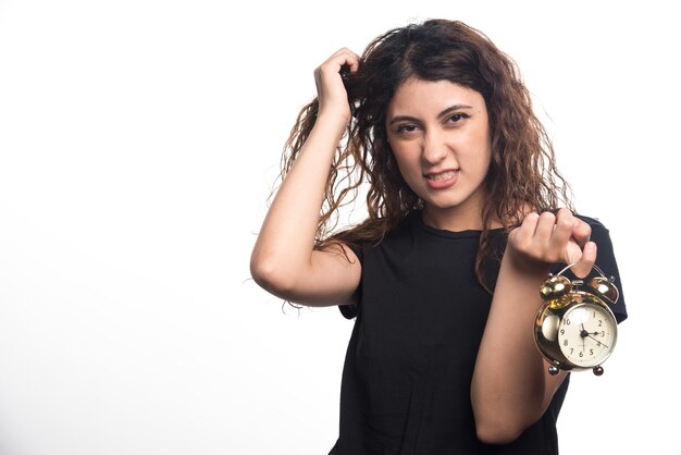 Mujer enojada sosteniendo su cabello y reloj sobre fondo blanco. Foto de alta calidad