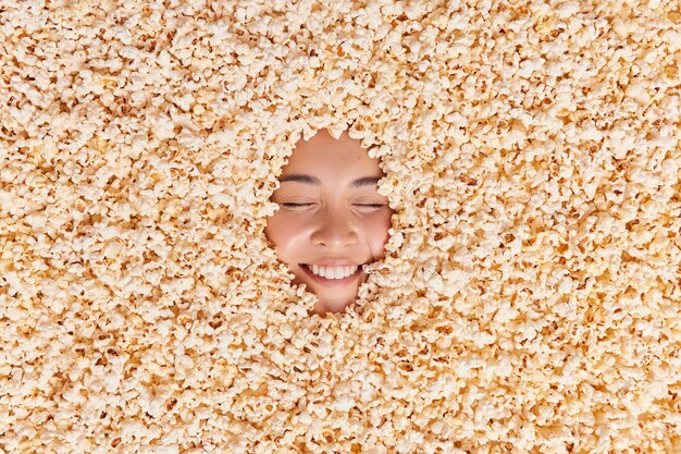 mujer enterrada en sabrosas palomitas de maíz sonríe alegremente muestra dientes blancos se siente alegre mientras ve una película de comedia