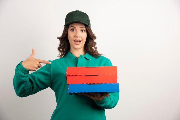 Mujer de entrega apuntando a cajas de pizza.