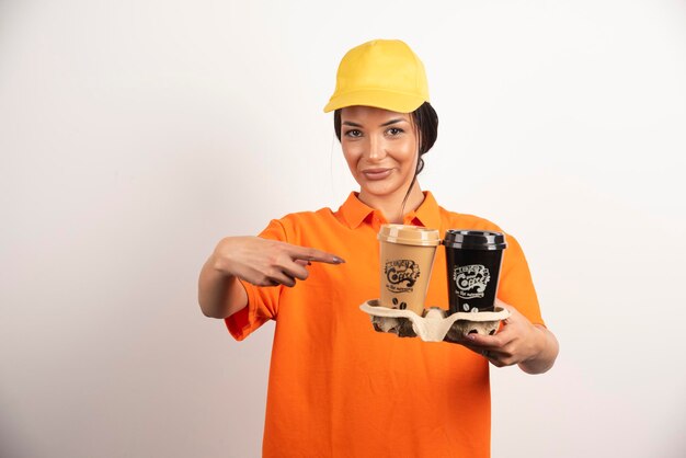 Mujer de entrega apuntando a tazas de café para llevar en la pared blanca.