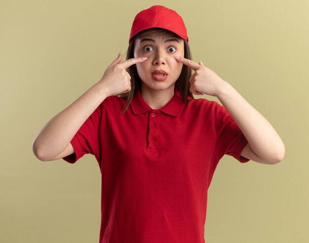 Mujer de entrega bonita ansiosa en uniforme pone los dedos en los párpados