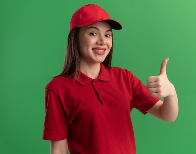 Mujer de entrega bonita complacida en uniforme pulgar hacia arriba en verde