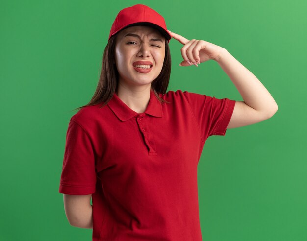 Mujer de entrega bonita disgustada en uniforme pone el dedo en la cabeza en verde