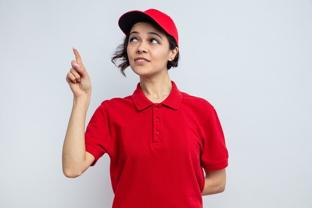 Mujer de entrega bonita joven complacida mirando y apuntando hacia arriba