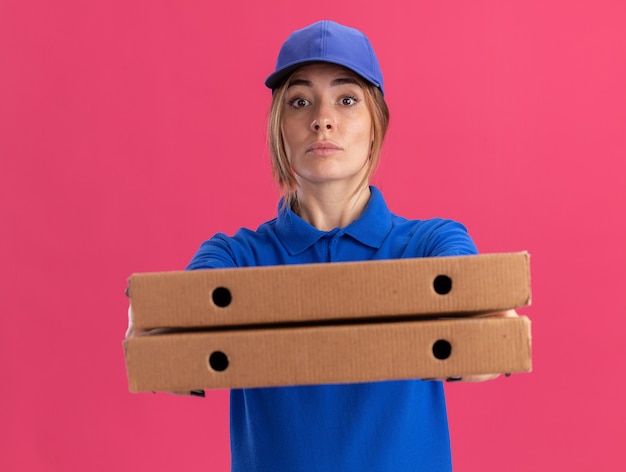 Mujer de entrega bonita joven confiada en uniforme tiene cajas de pizza aisladas