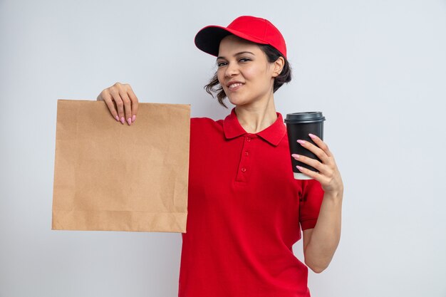 Mujer de entrega bonita joven contenta que sostiene el envasado de alimentos de papel y la taza de comida para llevar