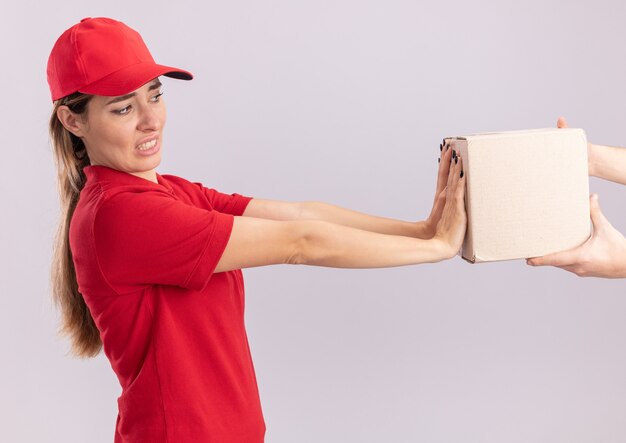 Mujer de entrega bonita joven descontenta en uniforme empujando cardbox alguien sosteniendo aislado en la pared blanca