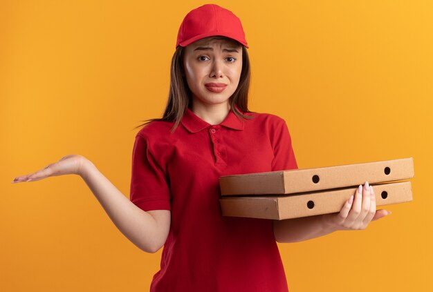 Mujer de entrega bonita triste en uniforme mantiene la mano abierta y sostiene cajas de pizza