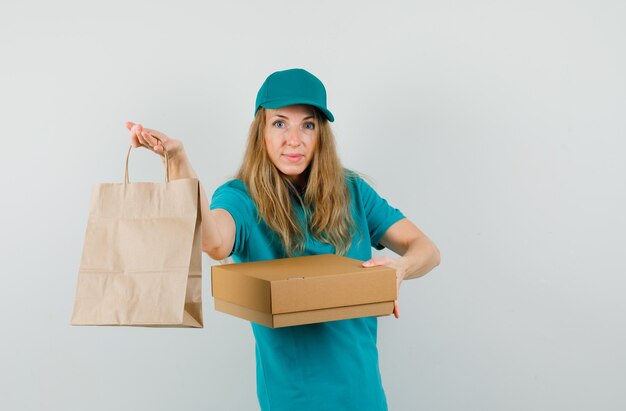 Mujer de entrega con caja de cartón y bolsa de papel en camiseta, gorra y alegre.