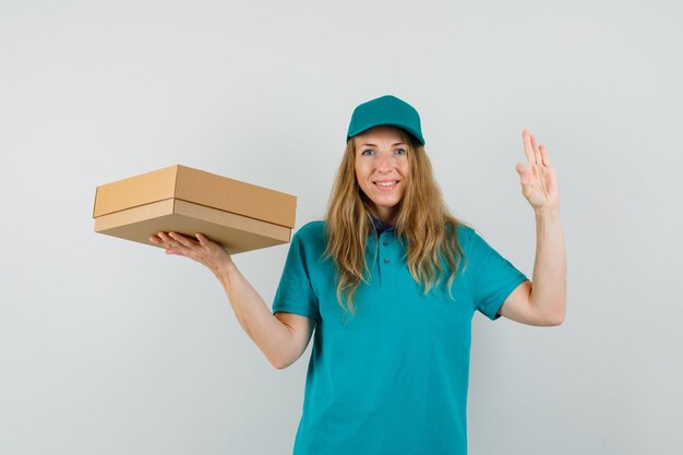 Mujer de entrega con caja de cartón con gesto ok en camiseta, gorra y mirando feliz