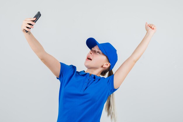 Mujer de entrega en camiseta azul y gorra tomando selfie mientras muestra gesto de ganador