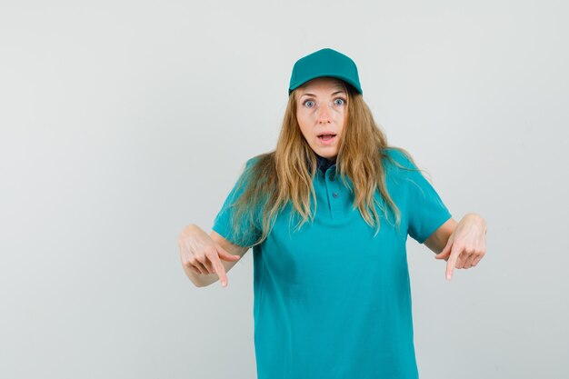 Mujer de entrega en camiseta, gorra apuntando hacia abajo y mirando sorprendido