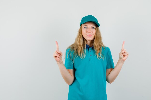 Mujer de entrega en camiseta, gorra apuntando hacia arriba y mirando positivo