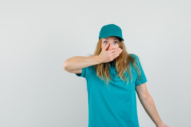 Mujer de entrega en camiseta, gorra cubriendo la boca con la mano y mirando asustada