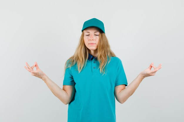 Mujer de entrega en camiseta, gorra haciendo meditación con los ojos cerrados y mirando tranquilo