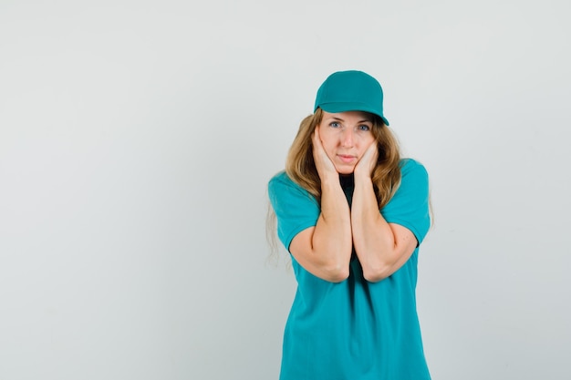 Mujer de entrega en camiseta, gorra juntando la cara con las manos y luciendo bonita