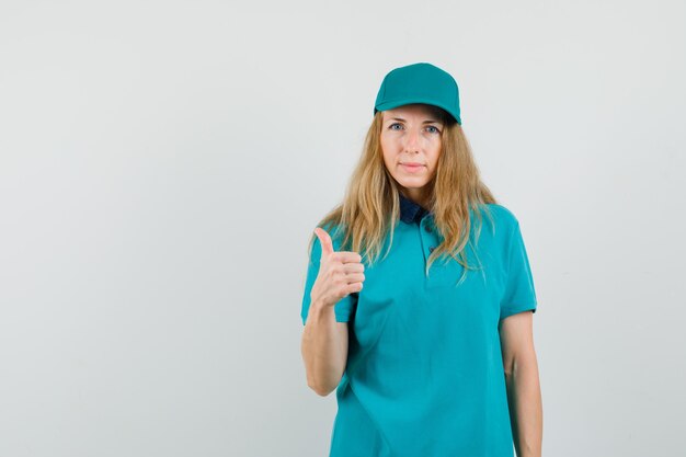 Mujer de entrega en camiseta, gorra mostrando el pulgar hacia arriba y mirando confiado