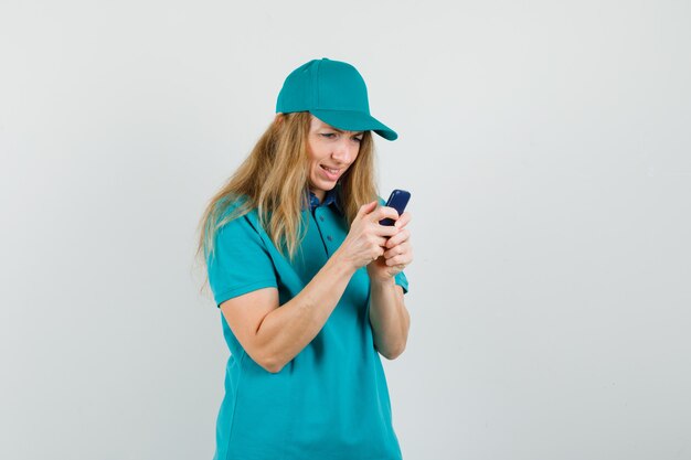 Mujer de entrega en camiseta, gorra con teléfono móvil y mirando confundido