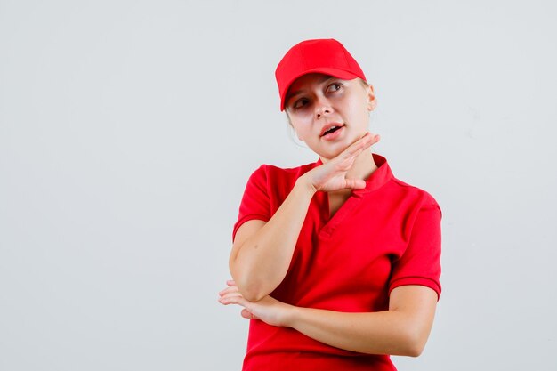 Mujer de entrega en camiseta roja y gorra apoyando la mano en la barbilla y mirando pensativo