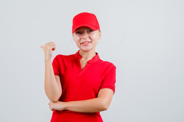 Mujer de entrega en camiseta roja y gorra apuntando hacia atrás y mirando alegre