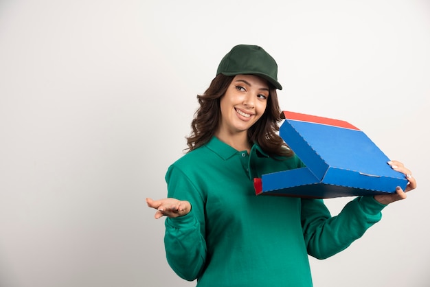 Mujer de entrega feliz en uniforme verde con caja de pizza abierta.