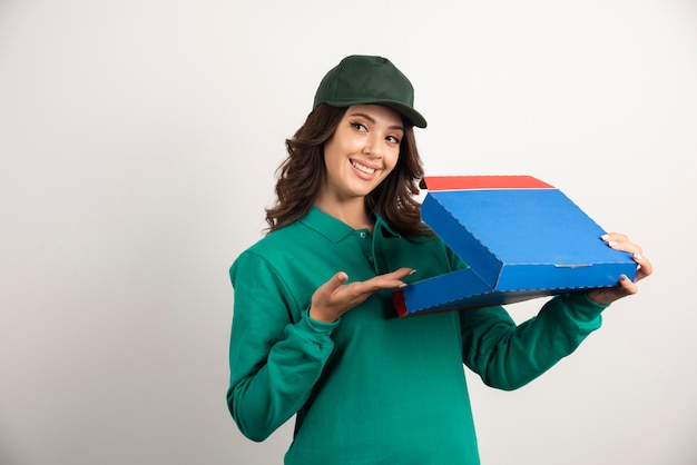 Mujer de entrega feliz en uniforme verde con caja de pizza abierta.