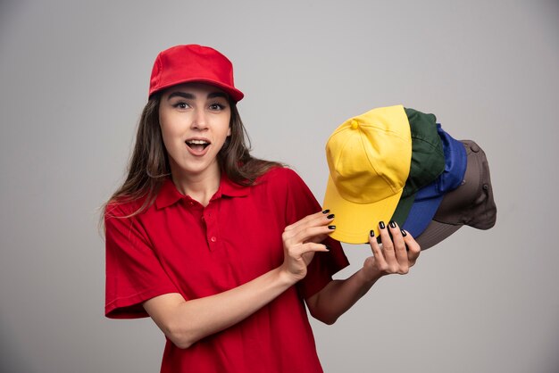 Mujer de entrega con gorras de colores posando en la pared gris.