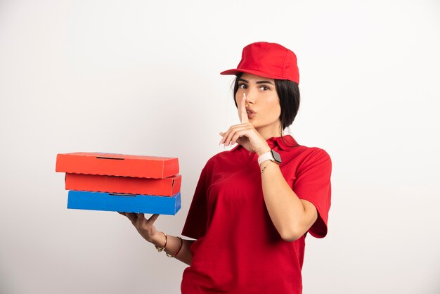 Mujer de entrega haciendo señal de silencio mientras sostiene la pizza.