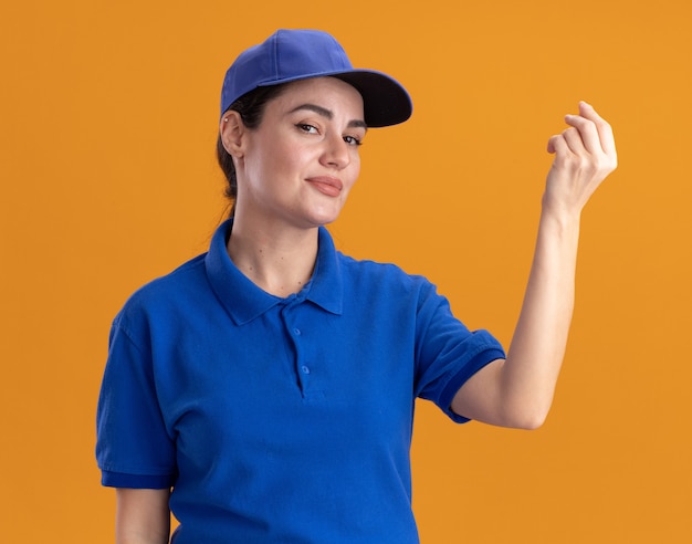 Foto gratuita mujer de entrega joven confidente en uniforme y gorra haciendo gesto de dinero