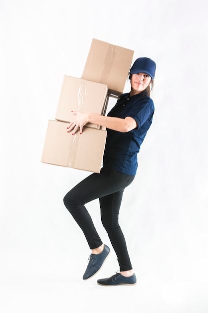 Mujer de entrega llevando apilados de cajas de mensajero contra el fondo blanco