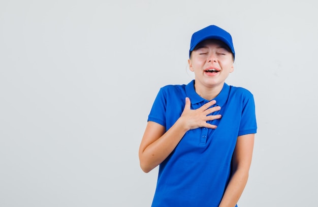 Mujer de entrega con la mano en el pecho en camiseta azul y gorra y mirando feliz