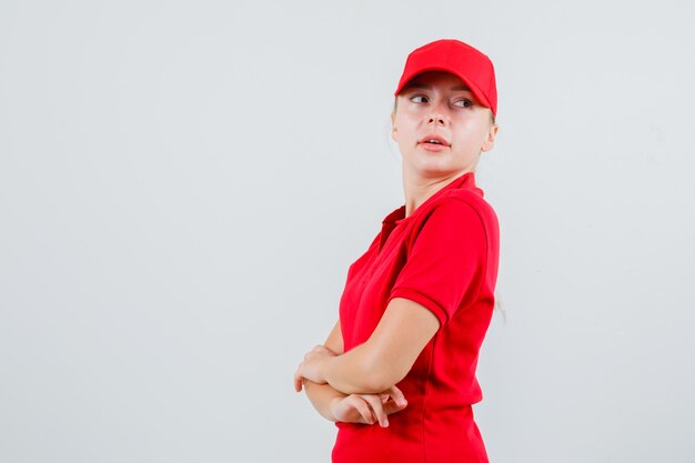 Mujer de entrega mirando hacia atrás con los brazos cruzados en camiseta roja y gorra y mirando curiosa. .