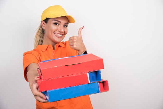 Mujer de entrega de pizza sosteniendo cajas de pizza haciendo pulgares hacia arriba sobre fondo blanco.