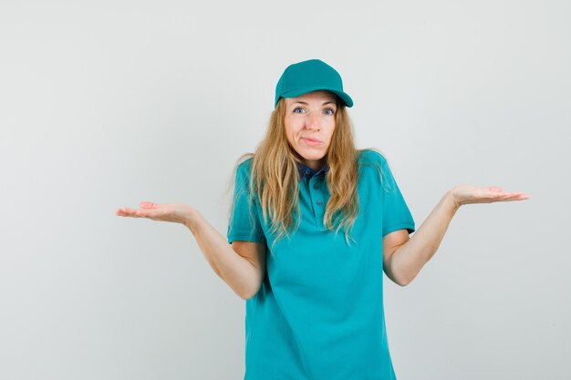 Mujer de entrega que muestra un gesto de impotencia encogiéndose de hombros en camiseta, gorra y mirando confundido