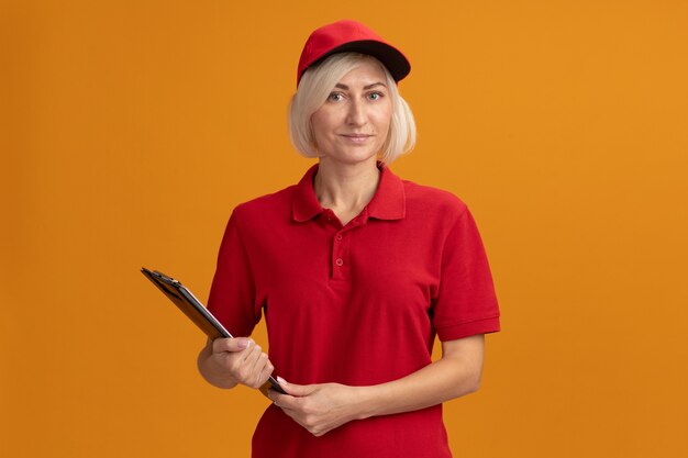 Mujer de entrega rubia de mediana edad complacida en uniforme rojo y gorra con portapapeles