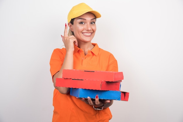 Mujer de entrega rubia sosteniendo cajas de pizza apuntando hacia arriba.