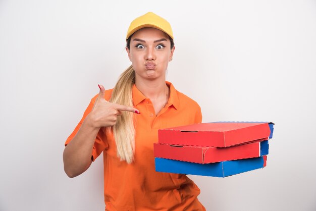 Mujer de entrega con sombrero amarillo señalando cajas de pizza.
