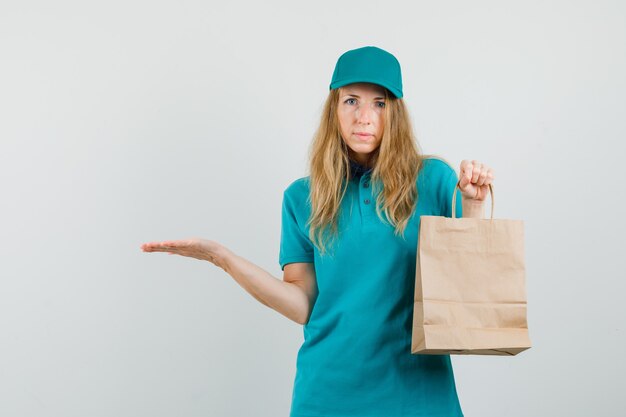 Mujer de entrega sosteniendo la bolsa de papel y extendiendo la palma a un lado en camiseta, gorra