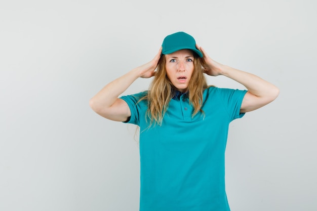 Mujer de entrega tomados de la mano a la cabeza en camiseta, gorra y mirando indefenso