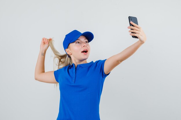 Mujer de entrega tomando selfie mientras sostiene el hilo en camiseta azul y gorra