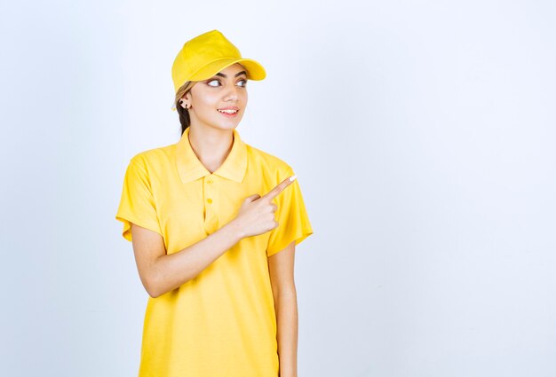 Mujer de entrega en uniforme amarillo de pie y apuntando hacia afuera con el dedo índice.