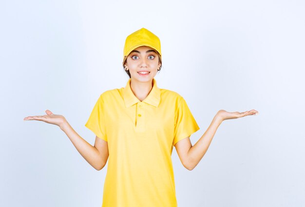 Mujer de entrega en uniforme amarillo de pie y encogiéndose de hombros.