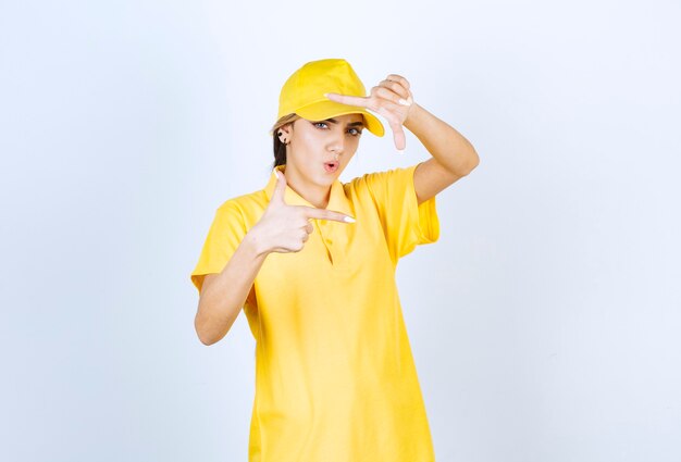 Mujer de entrega en uniforme amarillo de pie y haciendo marco con los dedos.