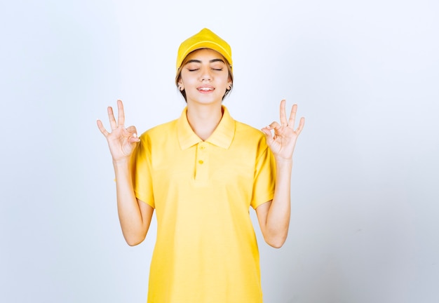 Mujer de entrega en uniforme amarillo de pie y meditando.